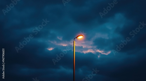 A streetlamp illuminates a dark, cloudy sky at dusk, creating a moody atmosphere.