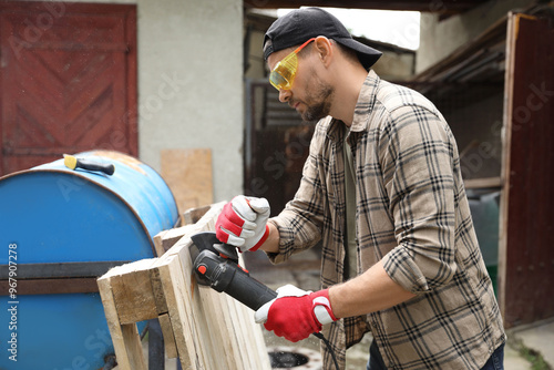 Man grinding wooden planks with angle grinder outdoors photo