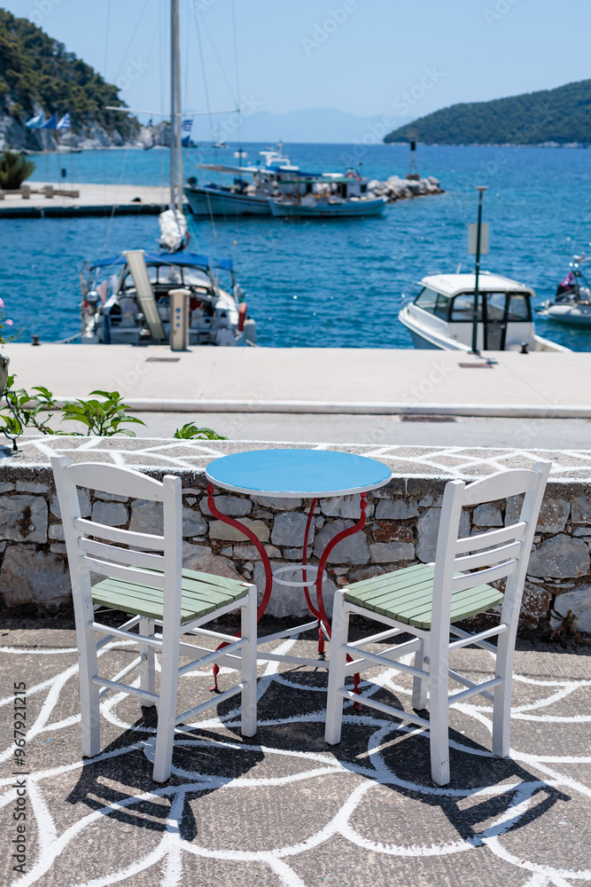 White chairs and a blue table overlooking a sunny harbor in Greece White chairs and a blue table overlooking a sunny harbor in Greece
