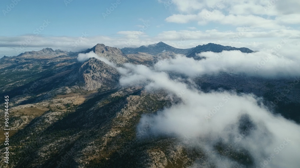 Aerial view of rugged mountains shrouded in clouds under a clear blue sky.