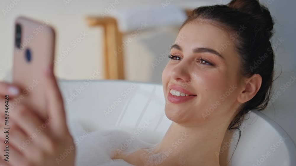 Smiling woman texting cellphone lying in bubble bath closeup. Cheerful brunette Smiling woman texting cellphone lying in bubble bath closeup. Cheerful brunette