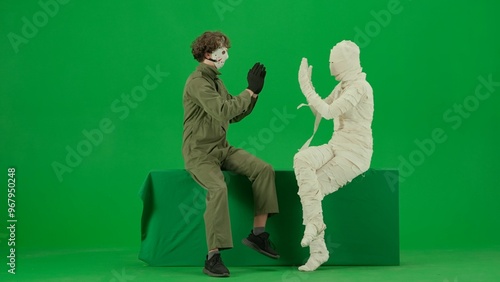 Portrait of person in a mummy bandage on chroma key green screen background. Mummy and maniac sitting playing clapping game, mummy confused. photo