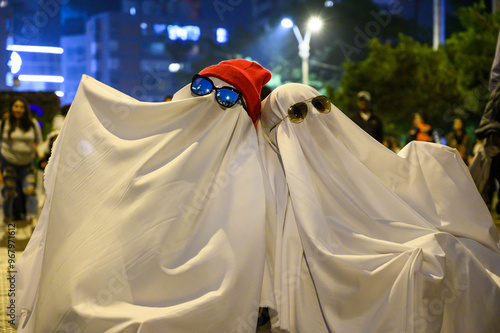 Two friends are having fun disguised as ghosts with sunglasses during a halloween party in the city