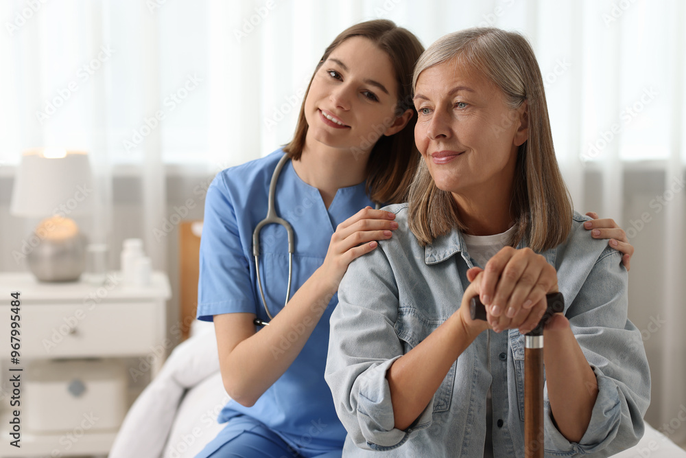 Fototapeta premium Smiling healthcare worker supporting senior patient on bed indoors. Space for text
