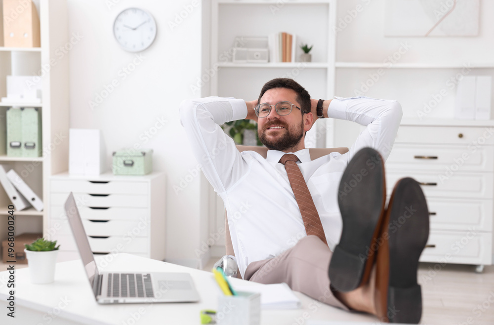 Smiling businessman with hands behind his head holding legs on table in office. Break time Smiling businessman with hands behind his head holding legs on table in office. Break time