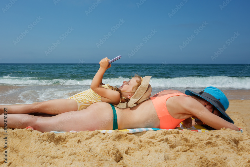 Mom and daughter enjoying beach day while using their phones Mom and daughter enjoying beach day while using their phones