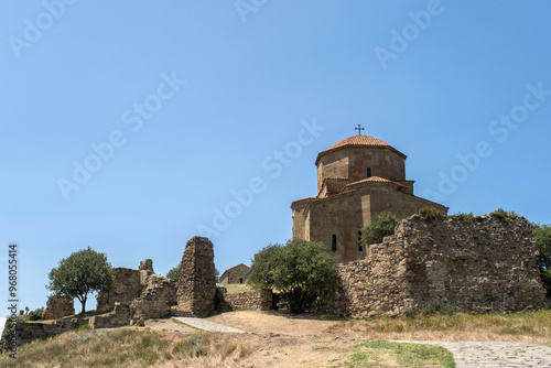 A weathered stone path winds its way through the ancient ruins of Jvari Monastery in Georgia. The iconic church stands tall above, a symbol of faith and history. photo