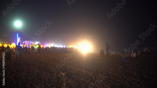 Slow panning shot showing crowd of people enjoying the night at a beach in goa maharastra with brightly lit shacks in the distance showing the vibrant nightlife photo