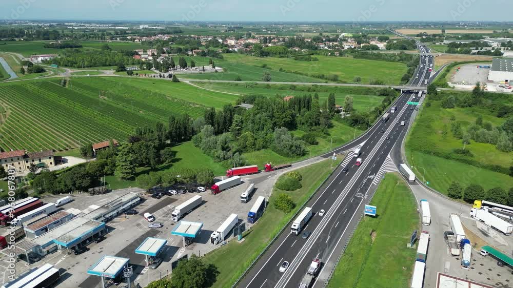 Aerial view of a busy motorway with a gas station and trucks surrounded by green fields, Cessalto, Italy. Aerial view of a busy motorway with a gas station and trucks surrounded by green fields, Cessalto, Italy.