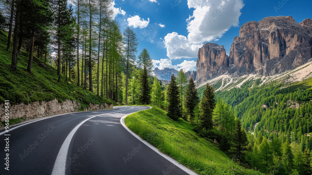 A winding road cuts through a lush green forest in the Italian Dolomites. Tall trees with thick leaves line the road, and towering rocks reach for the blue sky dotted with clouds.