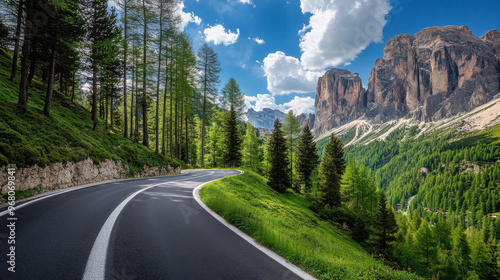 Obraz na płótnie A winding road cuts through a lush green forest in the Italian Dolomites. Tall trees with thick leaves line the road, and towering rocks reach for the blue sky dotted with clouds. w salonie