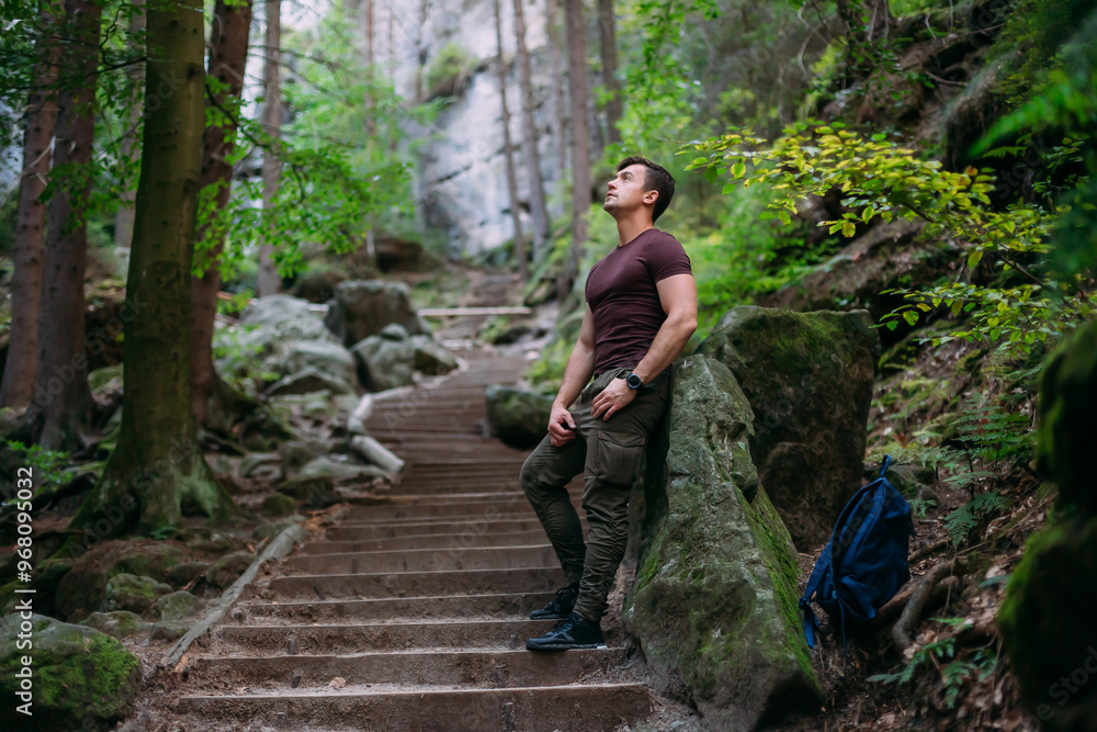 Young man on a stone staircase in the forest, leaning against a rock and thoughtfully looking upward, surrounded by greenery and trees. A serene and peaceful atmosphere in nature, perfect for outdoor Young man on a stone staircase in the forest, leaning against a rock and thoughtfully looking upward, surrounded by greenery and trees. A serene and peaceful atmosphere in nature, perfect for outdoor