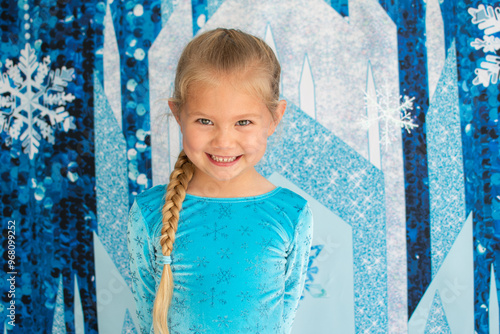Portrait of a cute smiling Caucasian little girl dressed up in a blue dress looking at the camera. Frozen theme costume. 