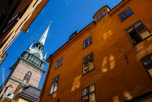 Photography A historic Riddarholmen church with a tall spire is framed by buildings in a cobblestone alleyway at Gamla stan in Stockholm