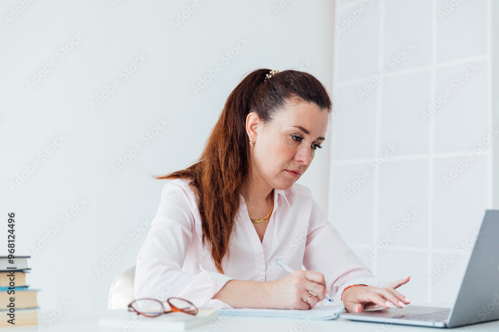 Beautiful business woman with online laptop at desk in office Beautiful business woman with online laptop at desk in office