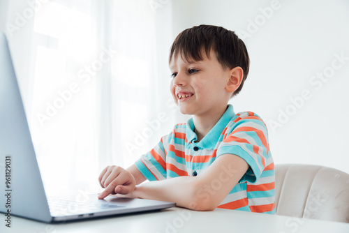 Boy schoolboy sitting at table with laptop online