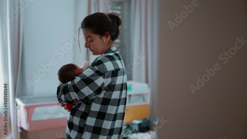 Mother holding her baby close, with a gentle expression, in a peaceful bedroom. The infant is wrapped in a soft blanket, feeling safe and loved