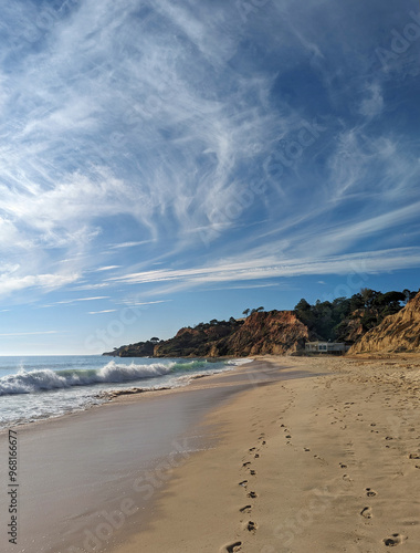 Summer weather on the beach in the Algarves Portugal with breaking waves, footprints in the wet sand and slopes at the coastline