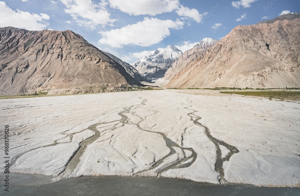 Fototapeta premium A panorama of the mountain landscape of the Wakhan Corridor and the Panj River in the valley with rocky mountain peaks with snow and glaciers in the background, in Tajikistan in Pamir