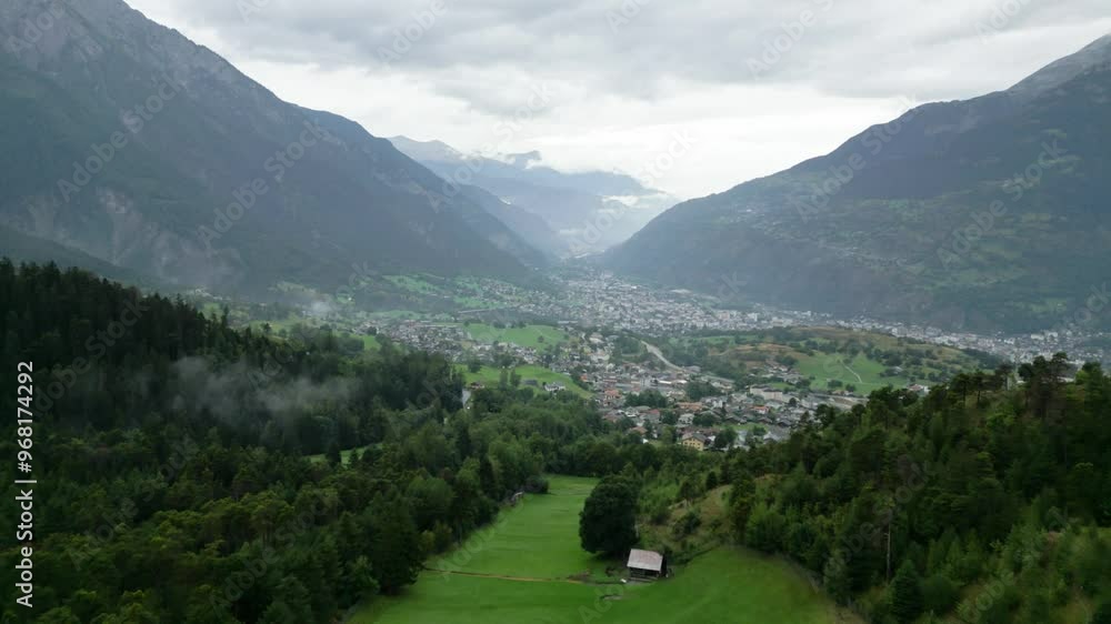 scenic aerial view from the top of mountain onto foggy and rainy valley with green grass and lodges (swiss mountains) b-roll scenic aerial view from the top of mountain onto foggy and rainy valley with green grass and lodges (swiss mountains) b-roll