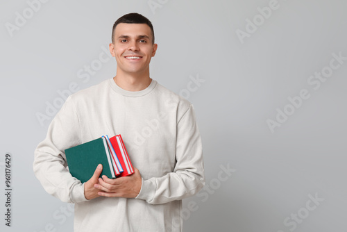 Handsome young man with books on grey background