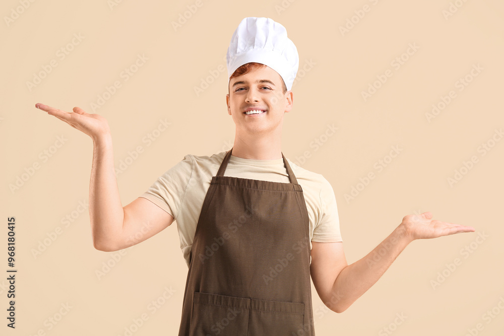 Male confectioner in apron pointing at something on beige background