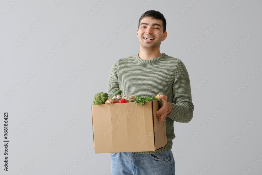 Happy young man with grocery box on grey background Happy young man with grocery box on grey background