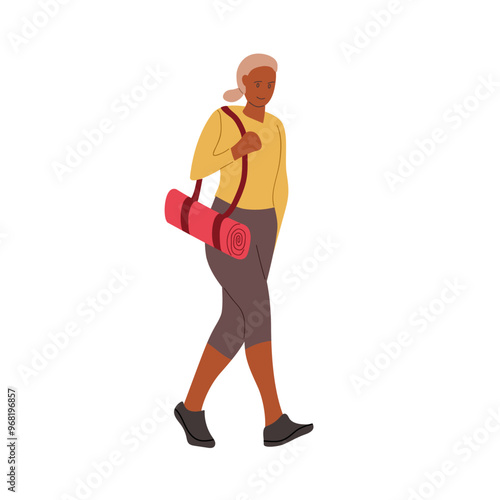 Woman walking with a yoga mat in a casual outfit during a sunny day outdoors