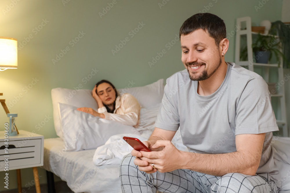 Obraz premium Young man texting mistress and his sleeping wife in bedroom at night. Cheating concept