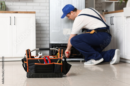 Male worker with tools repairing refrigerator in kitchen photo