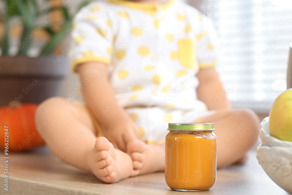 Cute little baby with jar of tasty food sitting in kitchen at home, closeup Cute little baby with jar of tasty food sitting in kitchen at home, closeup