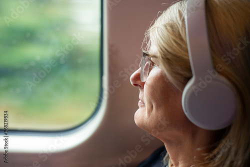 Woman sitting on a moving train listening to headphones,relaxing while looking out of a window,Worcestershire,United Kingdom.