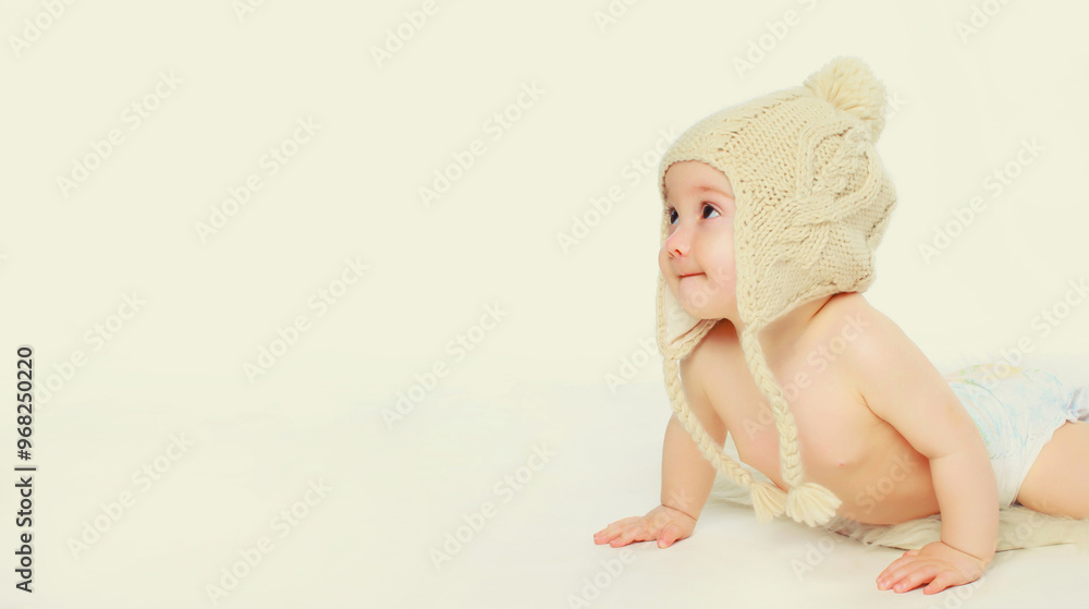 Happy baby in winter knitted hat crawling on the floor playing on white studio background Happy baby in winter knitted hat crawling on the floor playing on white studio background