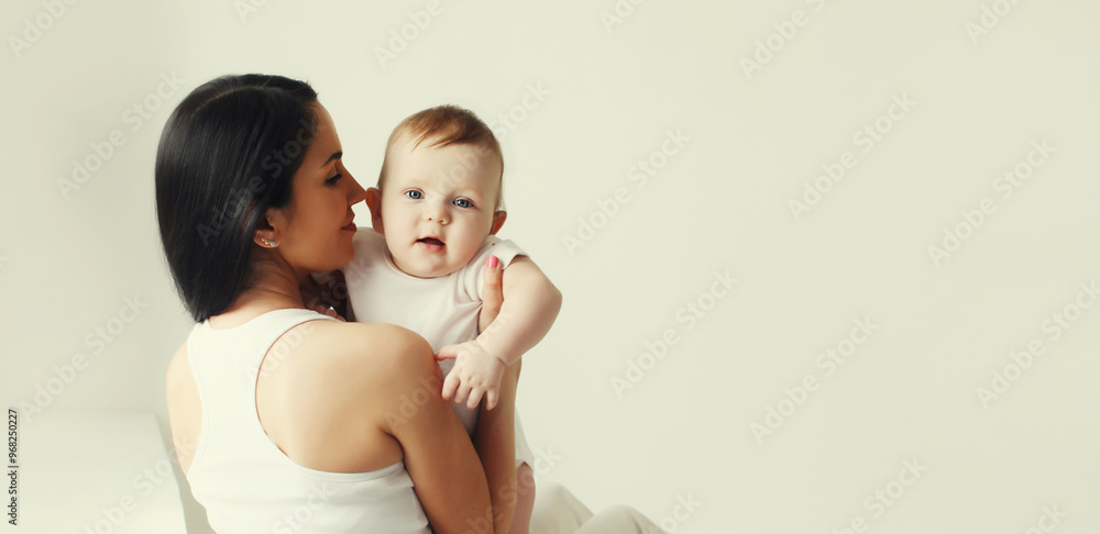 Happy young mother holding cute baby together in white room at home Happy young mother holding cute baby together in white room at home