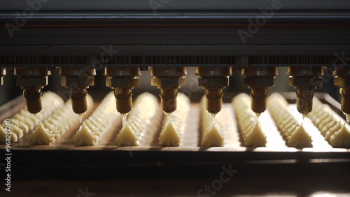 Machine pouring chocolate cream filling on cookies.