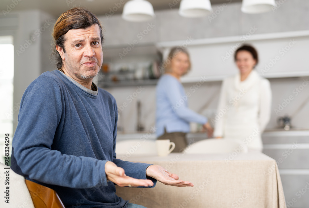 Fototapeta premium Distressed man is present during quarrel between his wife and elderly female mom. Mature woman and daughter-in-law swear and insult each other