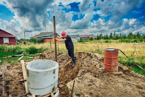 Builder places one concrete ring on top of another and levels it with lever using steel pipe when building septic tank. photo