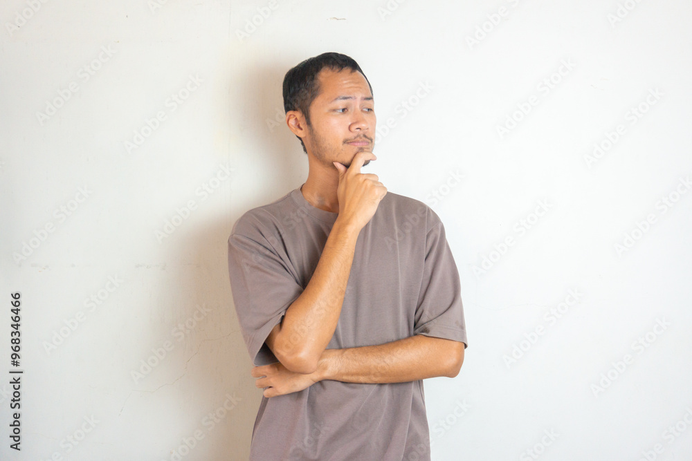Young Adult bearded Asian man wearing green flannel shirt showing thinking gesture. Hip on chin Young Adult bearded Asian man wearing green flannel shirt showing thinking gesture. Hip on chin