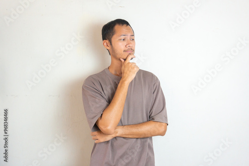 Young Adult bearded Asian man wearing green flannel shirt showing thinking gesture. Hip on chin