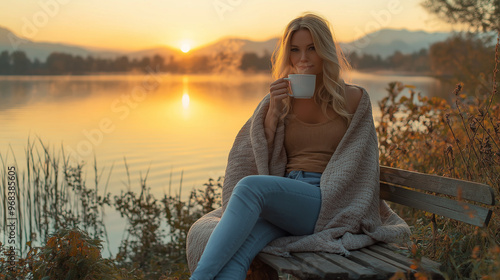 Fototapeta Naklejka Na Ścianę i Meble -  Woman enjoying a hot drink at sunrise by the lake