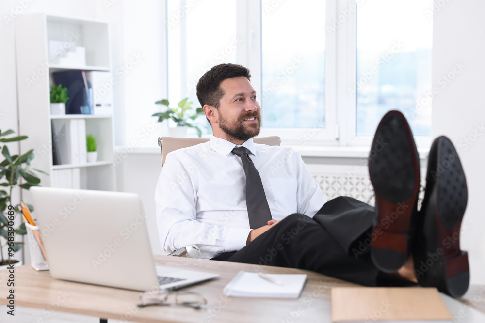 Smiling businessman holding legs on table in office. Break time Smiling businessman holding legs on table in office. Break time
