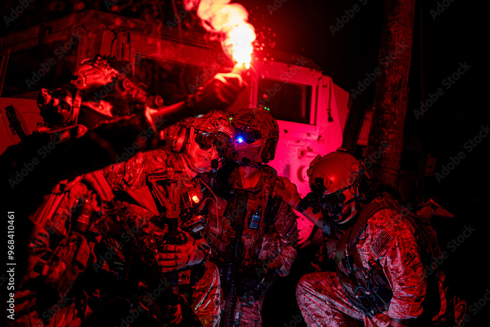 Obraz premium soldiers wearing combat gear gather around a flare during military operation. The dark setting and flare emphasize the stealth and readiness. soldiers using a red flare to strategize night mission.