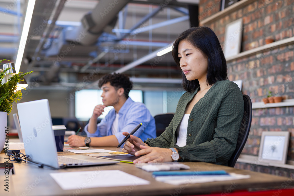 Working in modern office, asian woman using laptop and stylus for design work Working in modern office, asian woman using laptop and stylus for design work