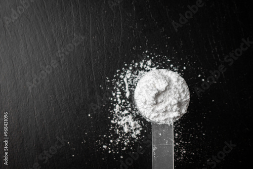 Creatine powder in a measuring scoop, pre-workout for gym on black wooden background.