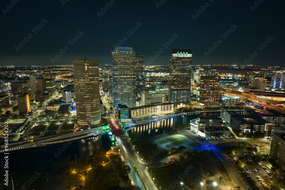 Fototapeta premium View from above of brightly illuminated high skyscraper buildings and moving traffic in downtown district of Tampa city in Florida, USA. American megapolis with business financial district at night