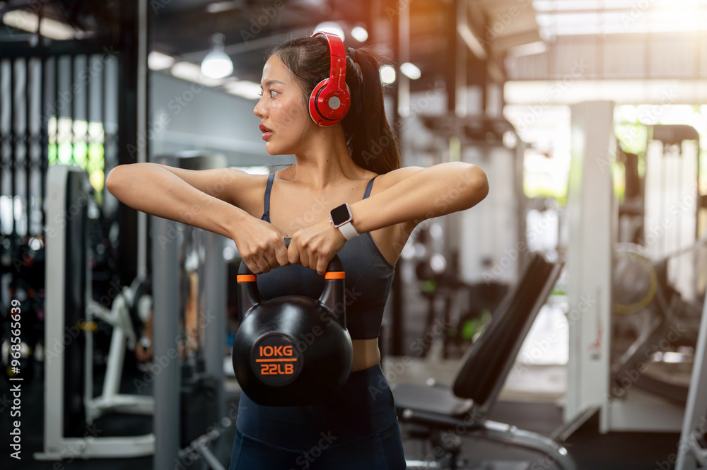 Fototapeta premium An attractive, sporty Asian woman is working out with a kettlebell at the gym.