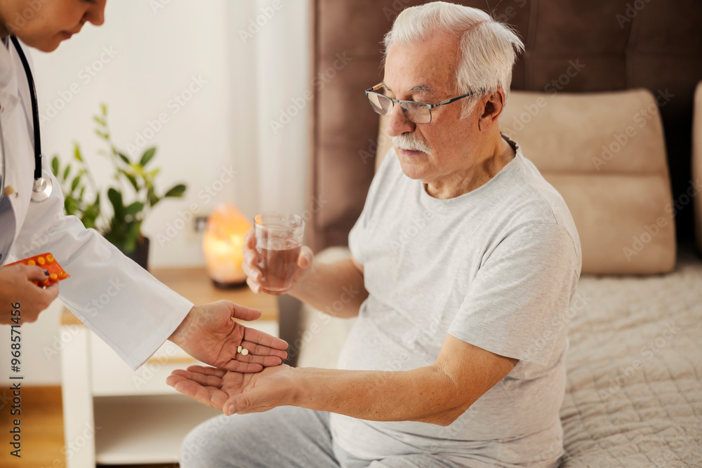 Senior man sitting on bed in bedroom and his doctor giving him painkillers. Senior man sitting on bed in bedroom and his doctor giving him painkillers.