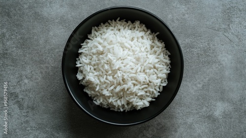 Minimalist top view of a black bowl filled with white rice, set against a grey background, perfect for food-related themes.