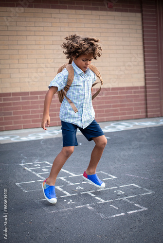 Foto Cute diverse African American school boy playing hopscotch on the school playground after school