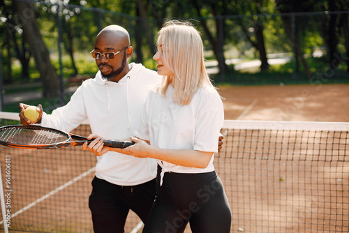 Black man teaching young woman to play tennis